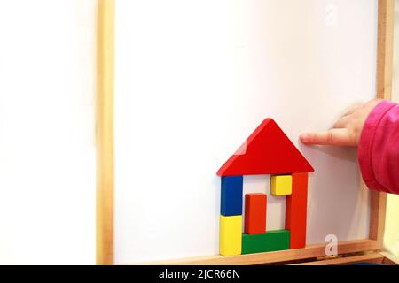 Kind spielt Holz magnetische pädagogische Spiel. Mädchen spielt mit einem Spielzeug auf weißem Hintergrund. Kind baut ein Haus aus einem Konstrukteur Stockfoto