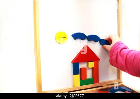 Kind spielt Holz magnetische pädagogische Spiel. Mädchen spielt mit einem Spielzeug auf weißem Hintergrund. Kind baut ein Haus aus einem Konstrukteur Stockfoto