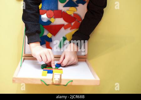 Kind spielt hölzerne magnetische pädagogische Spiele. Kinder spielen Mosaik. Blick von oben. Kind spielt mit einem Konstrukteur Stockfoto