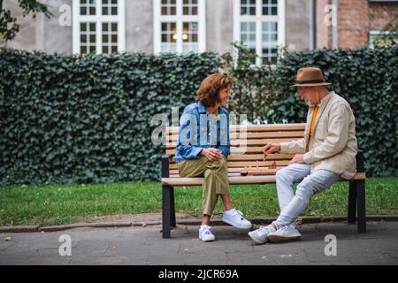 Glückliches Seniorenpaar, das auf der Bank sitzt und im Park Schach spielt. Stockfoto