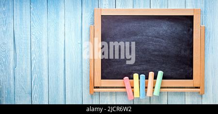 Kleine schwarze Tafel mit farbigen Kreiden auf blauen Holzplanken. Zurück zum Schulkonzept Stockfoto