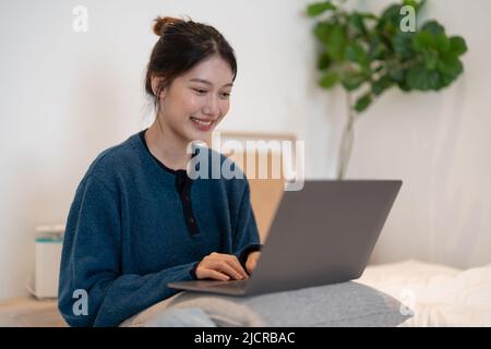 Asiatisches Mädchen, das von zu Hause aus auf einem Laptop arbeitet oder von zu Hause aus studiert oder freiberuflich tätig ist. Oder sie schaut sich ein Video an oder nutzt das Internet Stockfoto