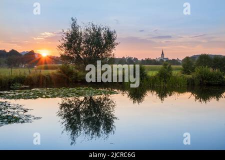 Sonnenuntergang an einem Teich. Im Hintergrund die Kirche St. Andreas in Teisendorf. Berchtesgadener Land, Oberbayern, Deutschland Stockfoto