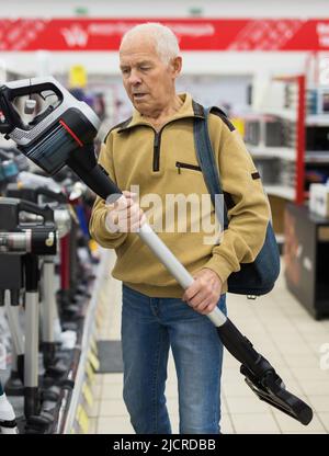 Älterer grauhaariger Rentner, der aufrechte vakuumsauger am Schalter im Ausstellungsraum der Abteilung für Elektrogeräte-Hypermarkt sucht Stockfoto