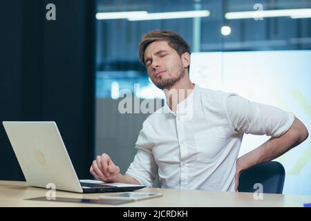 Junger Geschäftsmann, der im Büro arbeitet, hat müde Rückenschmerzen. Stockfoto