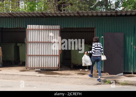 Hausfrau wirft Müll in einen Container im Hof des Hauses. Stockfoto