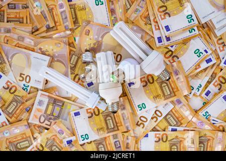 Hintergrund mit Euro-Banknoten und verschiedenen Glühbirnen, die die Stromkosten darstellen. Stockfoto
