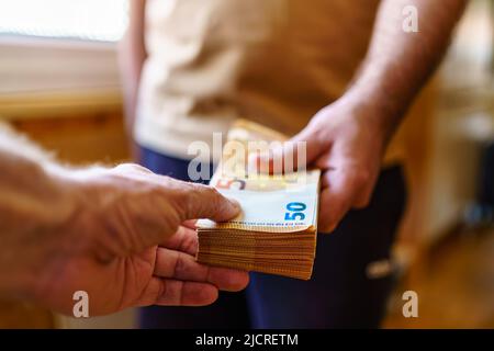 Mann, der einen Stapel Euro-Scheine hält und ihn an jemand anderen übergibt. Stockfoto