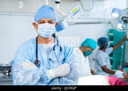 Portriat Aufnahme eines selbstbewussten Chirurgen im Operationssaal, der selbstbewusst mit gekreuzten Armen durch die Kamera steht - Konzept der medizinischen Versorgung, professionell Stockfoto