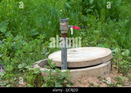 Technischer Betonbrunnen mit einem Rohr und einem Hebel für die Wasserversorgung. Konstruktion der Wasserversorgung Stockfoto