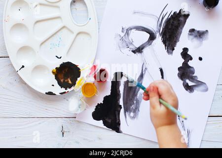 Blick von oben. Kind zeichnet einen Pinsel und malt Draufsicht. Flache Kunstwerkzeuge zum Malen. Stockfoto