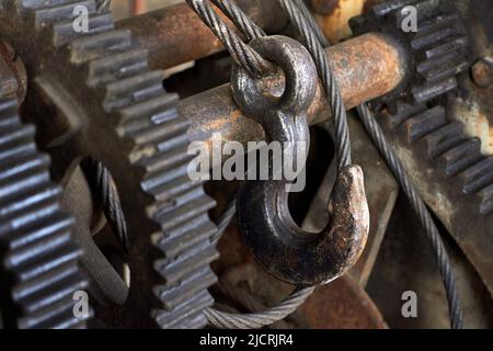 Haken für den Seilzug aus Stahl mit Zahnrädern. Drahtseilschlinge und Raupentrommel der Hebekranmaschine. Nahaufnahme selektiver Fokus industrieller Mechanismus Stockfoto