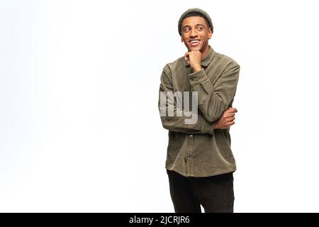 Nachdenklich lächelnder afroamerikanischer junger Mann im Hemd, verloren in Träumen, isoliert auf Weiß. Freundlicher, gut aussehender multirassischer Mann, der die Hand am Kinn hält und nach Inspiration oder neuen Ideen sucht Stockfoto