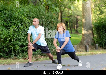 Reife Männer und Frauen, die sich als Paar in einer grünen natürlichen Umgebung des Stadtparks in Sportswear strecken Stockfoto