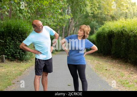 Zwei Erwachsene, die sich gegenseitig angucken, während sie nach dem Training in einem Stadtpark, umgeben von der Natur, ihren Körper streuen Stockfoto