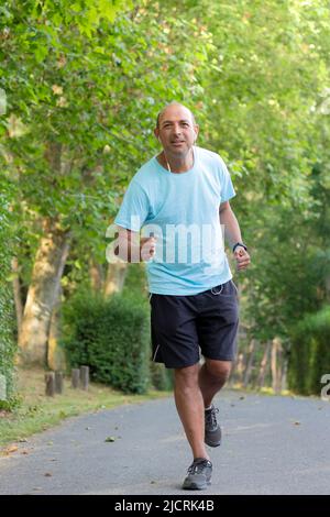 Frontportrait eines kahlen älteren Mannes, der durch den Park läuft und Sport macht, um sich in Form zu bringen und seinen Bauch zu schmal Stockfoto