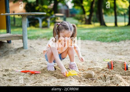 Schönes Baby mit Spaß an sonnigen warmen Sommertag - nettes Kleinkind Mädchen spielen im Sand auf Spielplatz im Freien Stockfoto