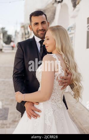 Gerade verheiratetes Paar, hübsche lockige blonde Frau, Braut und dunkelhaariger bärtiger Mann, Bräutigam, der zusammen steht. Frisch Vermählt Stockfoto