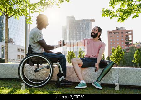 Multiethnische Menschen mit Behinderungen begrüßen einander im Freien - Fokus auf rechten Mann mit Beinprothese Stockfoto