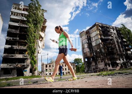 Borodjanka, Ukraine. 15.. Juni 2022. Eine Frau geht an zerstörten Wohngebäuden in Borodyanka vorbei. Russland hatte die Ukraine Ende Februar angegriffen, ohne den Krieg zu erklären. Besonders nach dem Abzug der Russen aus den nordwestlich von Kiew gelegenen Vororten Butscha, Irpin, Hostomel und Borodjanka hatten Bilder scheinbar hingerufene Menschen weltweit für Entsetzen gesorgt. Quelle: Kay Nietfeld/dpa/Alamy Live News Stockfoto