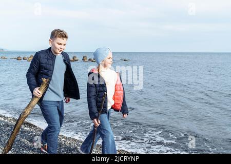 Kinder mit Stöcken auf einem Spaziergang am Meer. Stockfoto