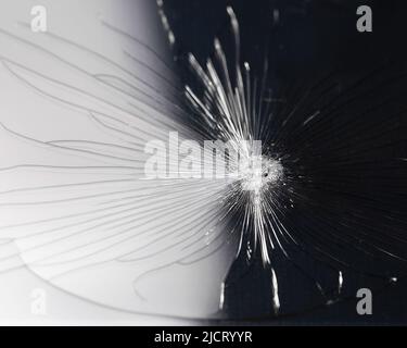 Gebrochener Glashintergrund mit Bullet-Loch auf schwarzem Hintergrund. Zerschmetterte und zerbrochene Glasstücke mit Lochglas. Makrofotografie. Telefon zerbrochenes Glas Stockfoto