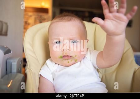 Ein mit Gemüsebrei verschmutztes Baby sitzt auf einem Kinderstuhl Stockfoto