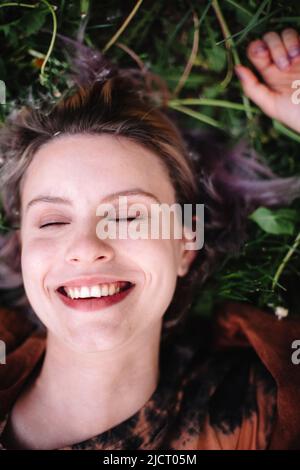 Porträt einer glücklichen jungen Frau, die im Frühjahr auf Gras liegt Stockfoto