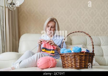 Eine Frau strickt mit ihren eigenen Händen Nadeln aus Wollgarn. Stockfoto