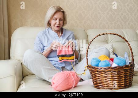 Eine Frau strickt mit ihren eigenen Händen Nadeln aus Wollgarn. Stockfoto