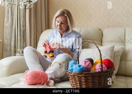 Eine Frau strickt mit ihren eigenen Händen Nadeln aus Wollgarn. Stockfoto