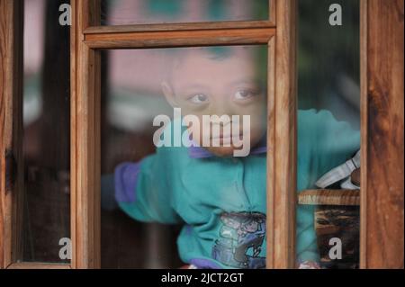 Mountain Province, Philippinen: Nahaufnahme eines jungen philippinischen Jungen in einem hellen Aqua-Pullover, der durch eine Fensterscheibe in einem Diner in Sagada guckt. Stockfoto