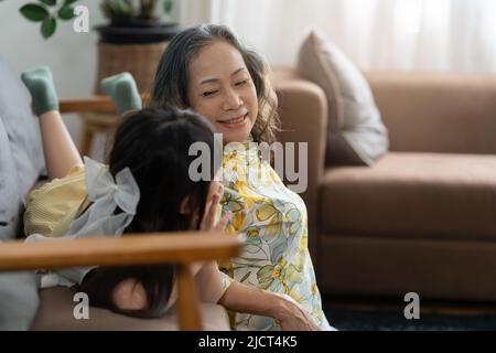 Glückliche Momente der asiatischen Großmutter mit ihrer Enkelin, die sich im Wohnzimmer zu Hause unterhielt. Stockfoto