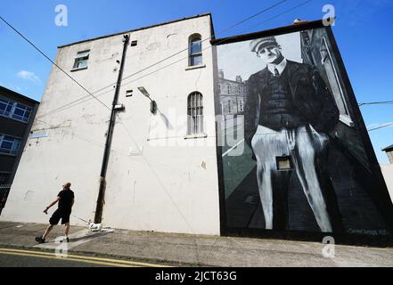 Ein Mann und ein Hund laufen vor dem Bloomsday an einem Wandbild von James Joyce von Shane Sutton Art in der Richmond Street North in Dublin vorbei. Bloomsday ist eine Feier des Lebens des irischen Schriftstellers James Joyce, der jährlich am 16. Juni, dem Tag, an dem sein Roman Ulysses aus dem Jahr 1922 im Jahr 1904 stattfindet, dem Datum seines ersten Ausflugs mit seiner Ehefrau Nora Barnacle, beobachtet wird. Der Tag ist nach seinem Protagonisten Leopold Bloom benannt. Bilddatum: Mittwoch, 15. Juni 2022. Stockfoto