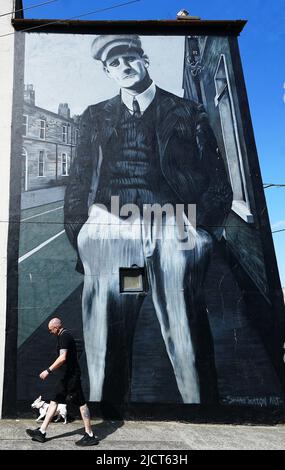 Ein Mann und ein Hund laufen vor dem Bloomsday an einem Wandbild von James Joyce von Shane Sutton Art in der Richmond Street North in Dublin vorbei. Bloomsday ist eine Feier des Lebens des irischen Schriftstellers James Joyce, der jährlich am 16. Juni, dem Tag, an dem sein Roman Ulysses aus dem Jahr 1922 im Jahr 1904 stattfindet, dem Datum seines ersten Ausflugs mit seiner Ehefrau Nora Barnacle, beobachtet wird. Der Tag ist nach seinem Protagonisten Leopold Bloom benannt. Bilddatum: Mittwoch, 15. Juni 2022. Stockfoto