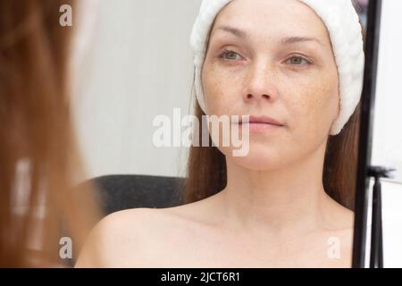 Lächelnde Frau mittleren Alters mit Band auf dem Kopf und Blick auf sich selbst im Spiegel Stockfoto