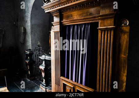 Typische alte hölzerne Beichtkabine an einer Kirche, mit blauen Vorhängen. Stockfoto