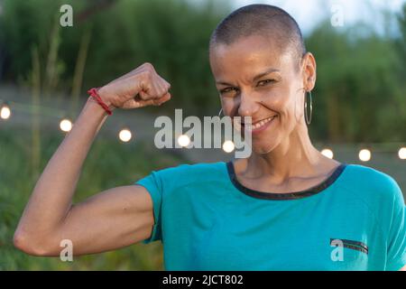 Starke Frau mit der Faust nach oben, rasierte Haare und ein großes Lächeln. Selbstbewusstes und starkes weibliches Nahaufnahme-Porträt. Stockfoto