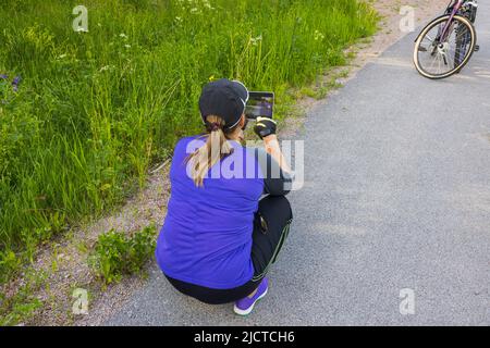 Nahaufnahme einer Frau, die sich am Straßenrand ausruhte und surfte, in der Nähe ihres Fahrrads. Schweden. Stockfoto