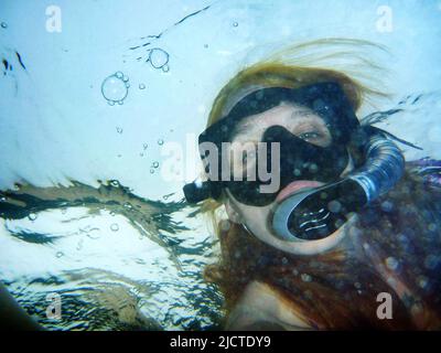 Frau mit Schnorchelmaske unter Wasser, die die Kamera anschaut Stockfoto