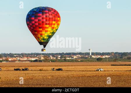 Coruche, Portugal - 13. November 2021: Großer Heißluftballon fliegt über Kornfelder und beobachtet Menschen auf einer Straße, in der Nähe von Coruche in Portugal, während der t Stockfoto