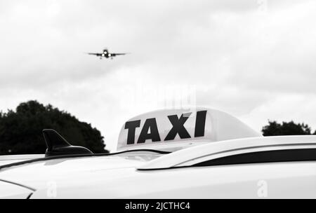 Nahaufnahme des Schildes auf einem Taxi auf einem Flughafen mit einem Flugzeug, das sich im Hintergrund nähert. Keine Personen. Schwarz und Weiß. Stockfoto