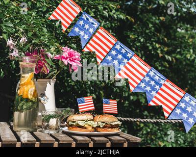 Zwei leckere Burger, hausgemachte Limonade, Vase mit hellen Blumen, Muster in Form von Sternen und Streifen. Nahaufnahme, im Freien. Tageslicht. Konzept o Stockfoto