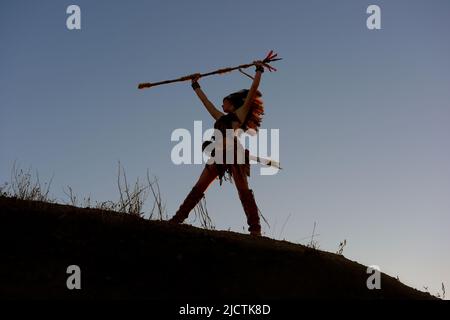 Ein junges Mädchen wird als Indianerin der Ureinwohner gesehen. Stolz posiert sie auf einem Hügel. Das indische Mädchen ist mit der untergehenden Sonne im Hintergrund verkümmelt. Stockfoto