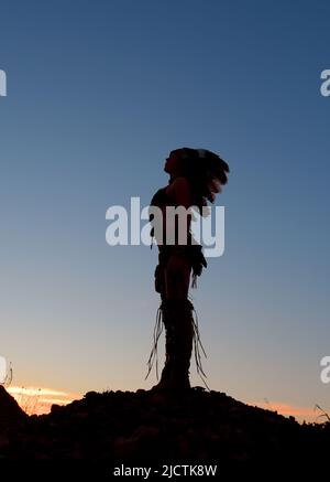 Ein junges Mädchen wird als Indianerin der Ureinwohner gesehen. Stolz posiert sie auf einem Hügel. Das indische Mädchen ist mit der untergehenden Sonne im Hintergrund verkümmelt. Stockfoto