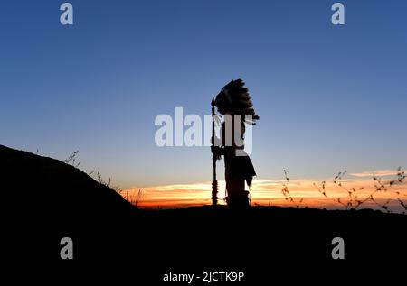 Ein junges Mädchen wird als Indianerin der Ureinwohner gesehen. Stolz posiert sie auf einem Hügel. Das indische Mädchen ist mit der untergehenden Sonne im Hintergrund verkümmelt. Stockfoto