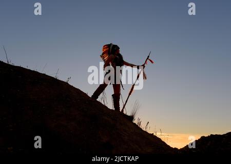 Ein junges Mädchen wird als Indianerin der Ureinwohner gesehen. Stolz posiert sie auf einem Hügel. Das indische Mädchen ist mit der untergehenden Sonne im Hintergrund verkümmelt. Stockfoto