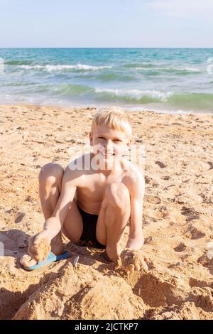 Sommerferien an der Küste. Ein Junge in Badehosen spielt im Sand am Strand, eine fröhliche Kindheit. Stockfoto