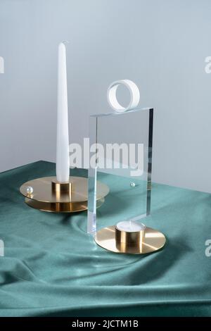 Kreative Stillleben Komposition mit Sojakerze auf pastellfarbenem Hintergrund, Kerzenhalter und eleganten Accessoires. Glas und Transparenz Stockfoto