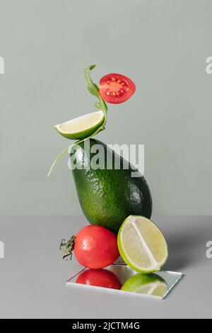 Frisches grünes Gemüse und Obst auf dem Tisch. Schwimmende Lebensmittelbalance mit Tomaten, Avocado, Kalk. Kreative trendige gesunde Lebensmittel und Kräuter für die Ernährung Stockfoto